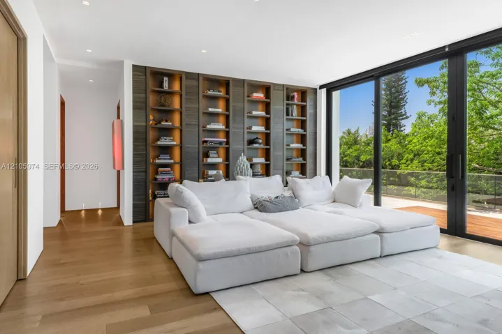 Custom floor-to-ceiling built-in shelving with integrated warm lighting, wide-plank wood-finish flooring, and expansive floor-to-ceiling sliding glass doors opening to a deck