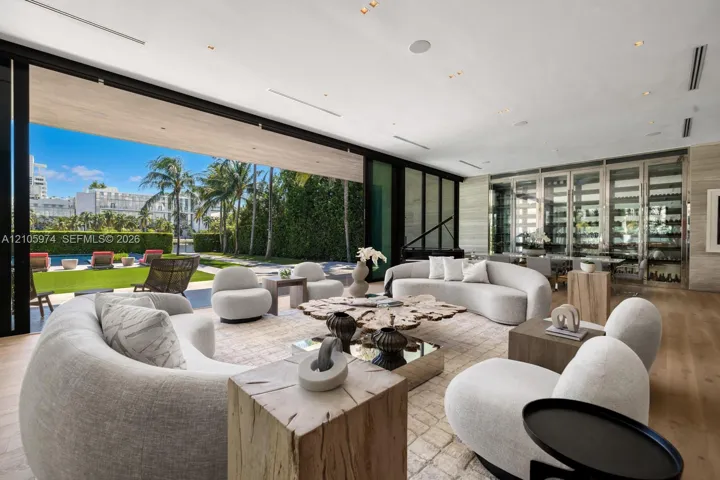 Floor-to-ceiling glass retractable wall, wide-plank wood-finish flooring, custom glass-enclosed wine storage, recessed lighting, and expansive stone wall cladding