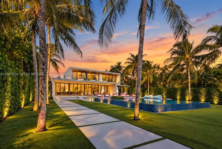Modern architectural exterior featuring floor-to-ceiling glass wall systems, a second-story balcony with metal railings, a tiled infinity-edge pool, and concrete paver hardscaping