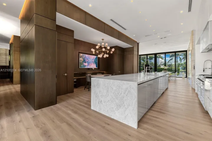 Large kitchen featuring a waterfall-edge stone island, wood-panel wall treatments, wood-finish flooring, a multi-globe chandelier, and expansive sliding glass doors