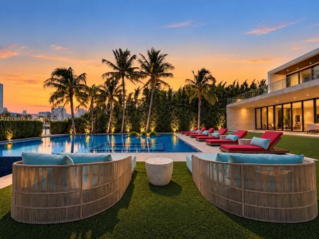 Outdoor living space featuring an inground swimming pool with stone tiling, synthetic grass lawn, perimeter hedges, and a glass-railed second-level balcony