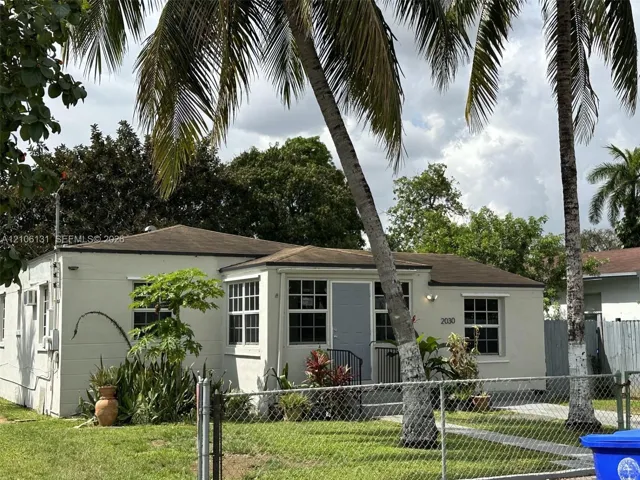 Single-story exterior featuring light-toned masonry, multi-pane windows, a low-pitch roof, and mature palm trees