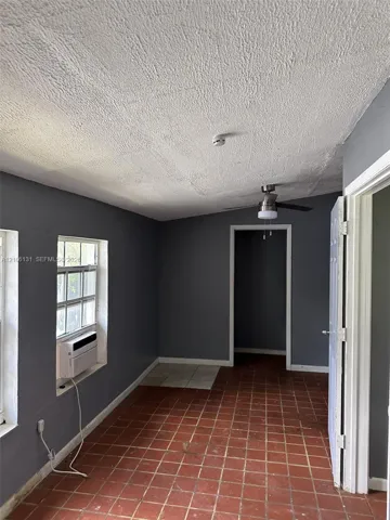 Room featuring red clay tile flooring, gray-toned wall finish, ceiling fan with integrated lighting, and multiple windows