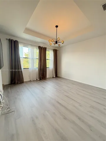 Tray ceiling with central multi-globe chandelier, wood-finish flooring, and expansive windows