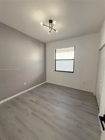 Interior room featuring wood-finish flooring, a multi-arm modern light fixture, a single window, and dual-panel closet doors