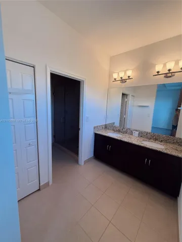 Bathroom featuring a dual-sink vanity with stone-finish countertop, dark cabinetry, large wall-mounted mirror, and tile flooring