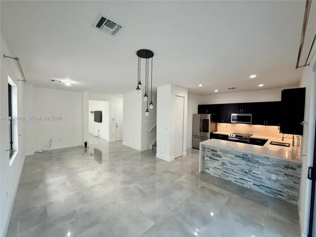 Open-concept area featuring oversized neutral tile flooring, kitchen with dark cabinetry, stone-veneer breakfast bar, and industrial-style pendant lighting