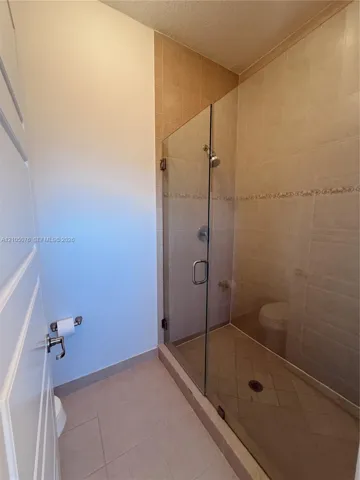 Walk-in shower enclosure with frameless glass door, neutral ceramic tile surround, integrated decorative tile inlay, and chrome finish hardware