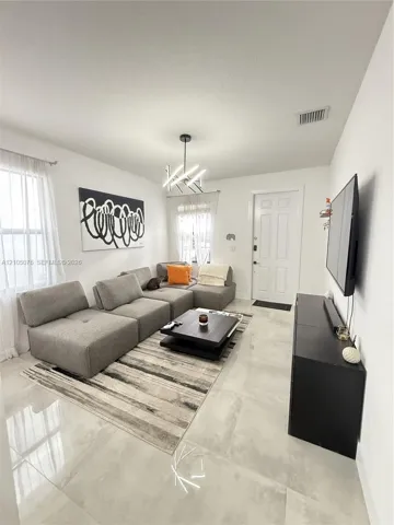 Living area featuring large-format light-toned tile flooring, multi-paned windows, and a contemporary geometric chandelier