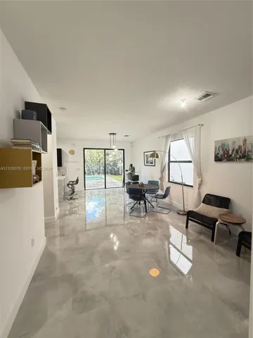 Open-concept interior featuring large-format tile flooring, recessed lighting, built-in wall shelving, and sliding glass doors revealing a swimming pool