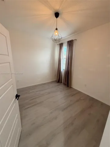 Room featuring wood-finish flooring, a geometric pendant light fixture, and a single-panel interior door with matte black hardware