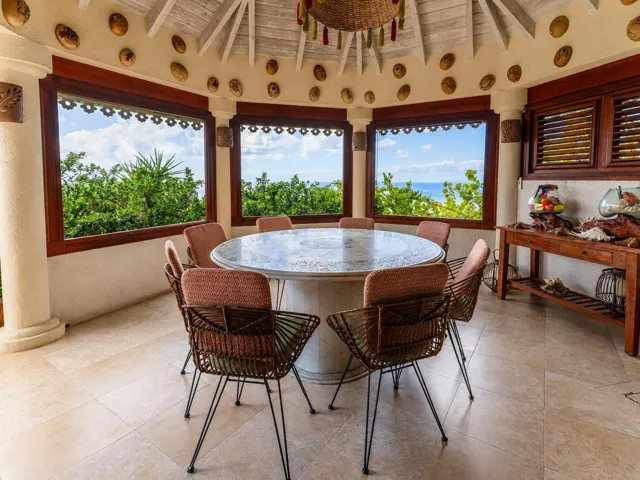 Charming dining area surrounded by large windows offering beautiful tropical views.