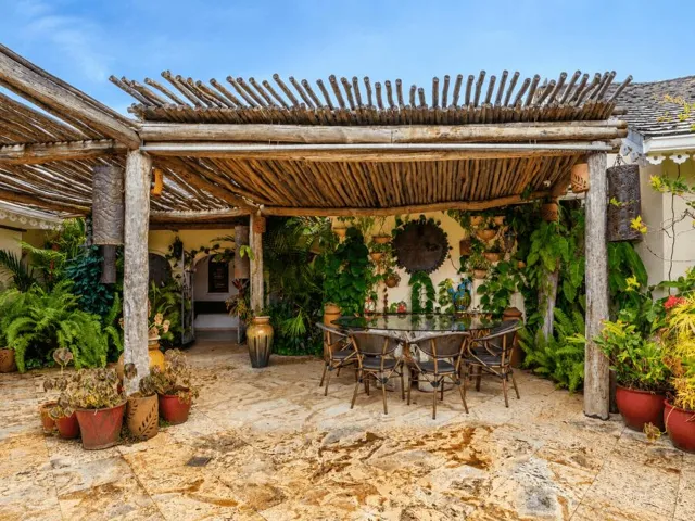 Charming covered patio featuring pergola-style roofing, outdoor seating, and lush greenery.
