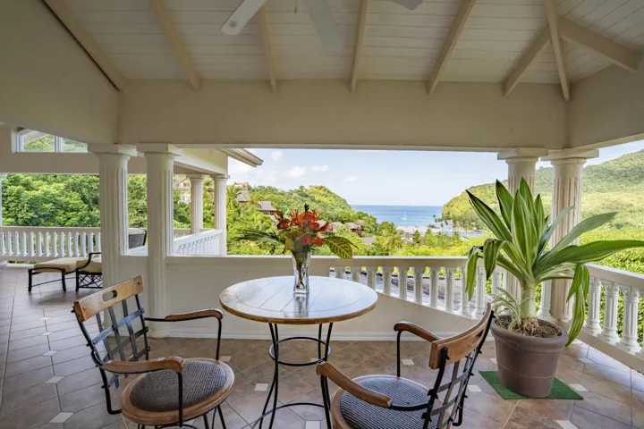Charming covered balcony with outdoor dining furniture and panoramic green views.