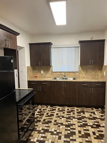 Kitchen featuring dark wood-finish cabinetry, stone-texture backsplash, dual-basin stainless steel sink with pull-down faucet, and rectangular flush-mount ceiling lighting
