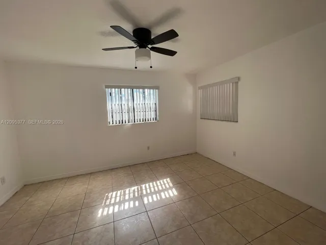 Neutral wall tones, ceramic tile flooring, matte black ceiling fan with integrated lighting, and vertical window blinds