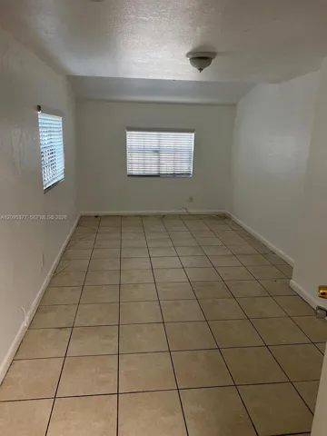 Interior room featuring large-format ceramic tile flooring, neutral wall finishes, and two windows equipped with horizontal blinds, illuminated by a flush-mount ceiling fixture