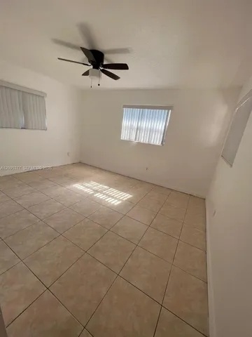 Neutral-toned tile flooring, dual windows with vertical blinds, and a matte black ceiling fan with integrated lighting