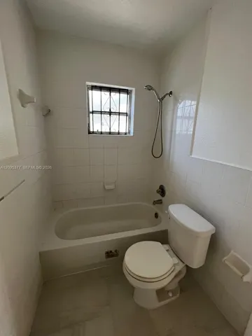 Full-height tiled walls, porcelain bathtub with a handheld shower fixture, and a window with security bars