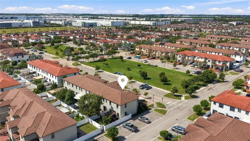 Aerial perspective of a multi-story residence with a clay tile roof, situated in a community featuring expansive green space and dedicated parking areas