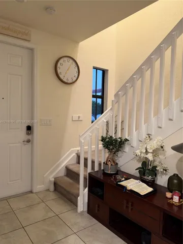 Entryway featuring ceramic tile flooring, a painted white staircase with a vertical balustrade, carpeted stair treads, and a multi-pane window