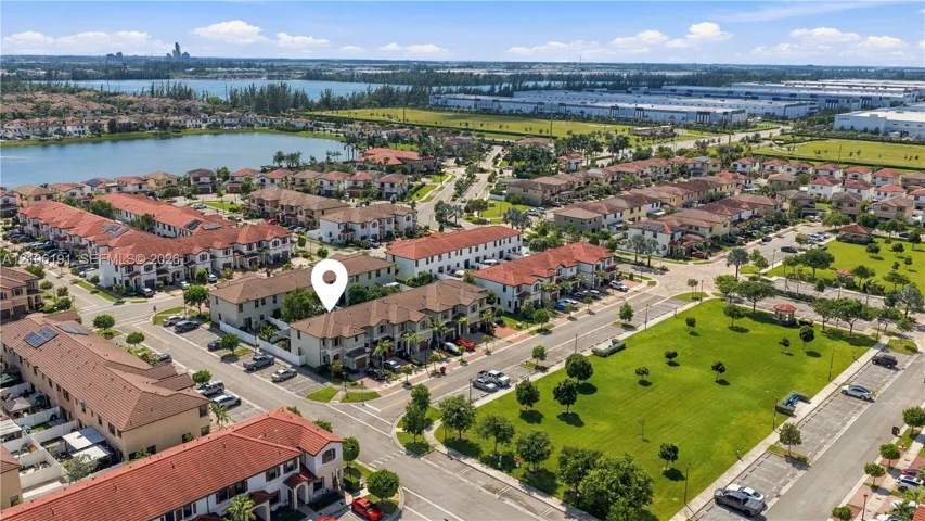 Aerial perspective of residential community featuring Mediterranean-style architecture with terracotta roof tiles, paved street grid, and proximity to a lake and landscaped green spaces