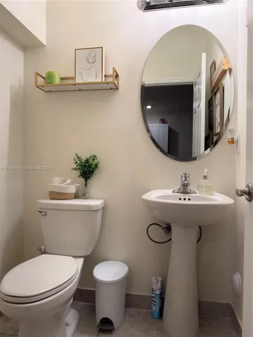 Pedestal sink with a single-handle faucet, oval wall-mounted mirror, and wall-mounted metal shelf