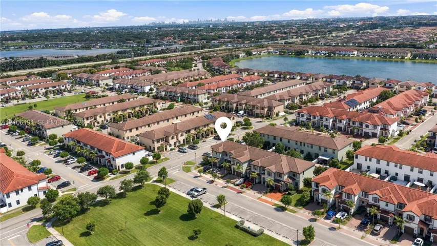 Aerial perspective of a multi-story residence featuring a terracotta-tiled roof and stucco exterior, situated within a community highlighted by expansive water frontage and manicured green spaces