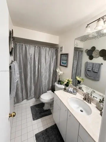 Bathroom featuring a vanity with an integrated oval basin and solid-surface countertop, a multi-bulb vanity light fixture, a large wall-mounted mirror, and tile flooring