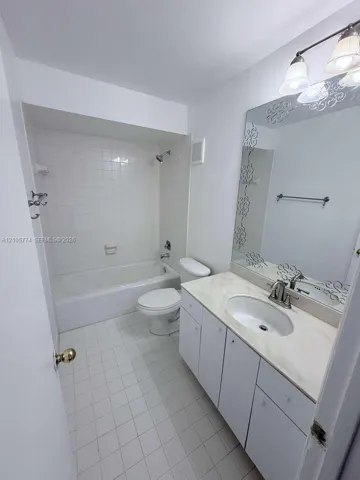 Bathroom featuring a vanity with an integrated countertop, oval sink, decorative mirror, three-light fixture, and a tiled shower-tub combination