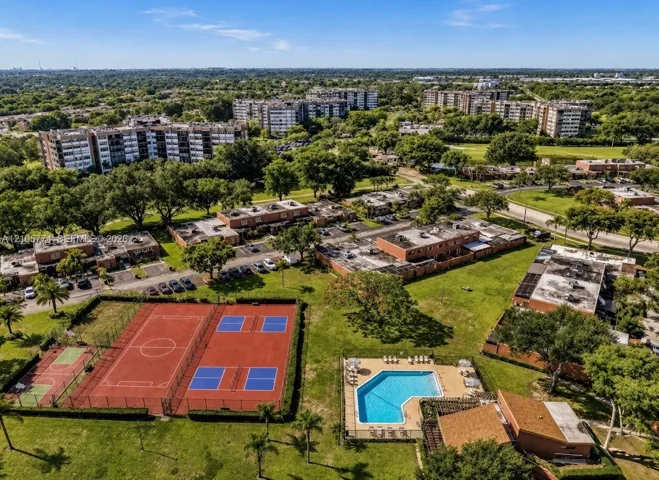 Aerial perspective of the property featuring a fenced swimming pool, multi-use sports courts, expansive manicured grounds, and mature tree canopy