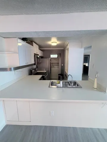 Kitchen featuring white cabinetry, solid-surface countertops, stainless steel sink with metal faucet, and wood-finish flooring