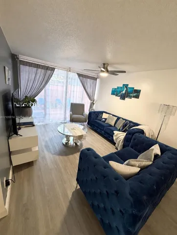 Living space featuring light wood-finish flooring, a ceiling fan with integrated lighting, and sliding glass doors with an accent wall