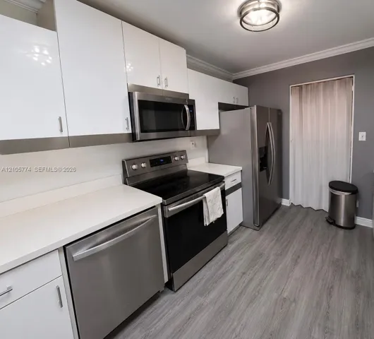 Kitchen featuring white cabinetry, solid-surface countertops, stainless steel appliances, and wood-finish flooring