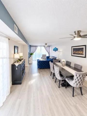 Open-concept living space featuring wood-finish flooring, recessed ceiling accent wall, dual brushed-metal ceiling fans, and sliding glass doors