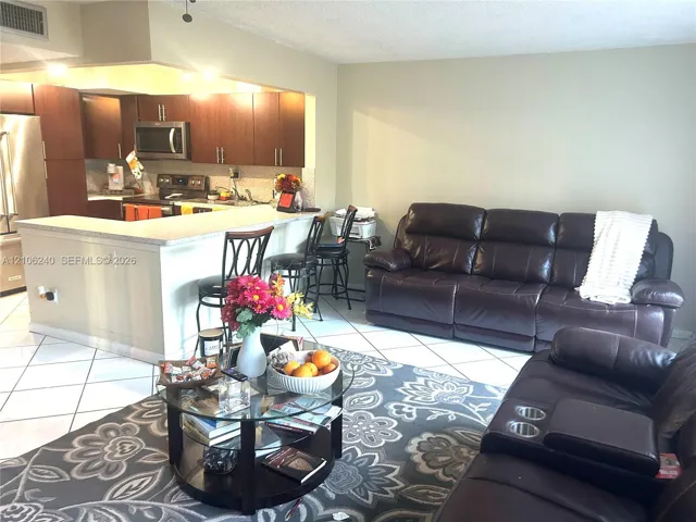 Kitchen featuring wood cabinetry, stone-surface breakfast bar, and stainless steel appliances, complemented by tile flooring