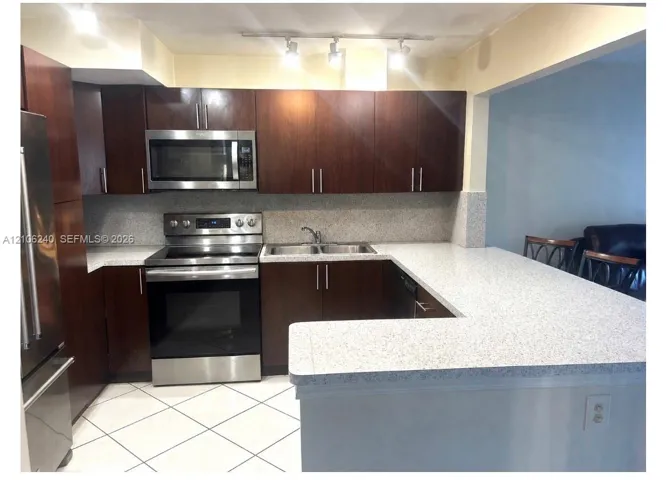 Kitchen featuring dark wood-finish cabinetry, speckled countertops, stainless steel appliances, a peninsula, and tile flooring