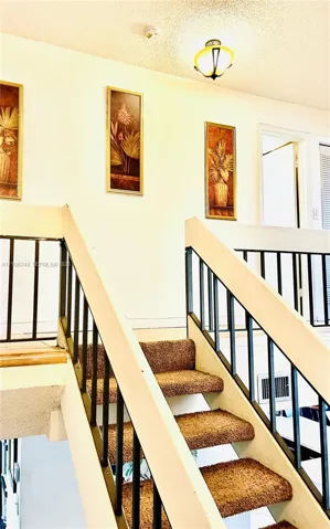 Staircase featuring carpeted treads and metal balustrades, complemented by a flush-mount ceiling light fixture