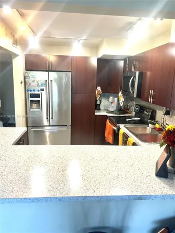 Kitchen featuring dark wood-finish cabinetry, stainless steel appliances, speckled stone-composite countertops, a dual-basin stainless steel sink, and track lighting