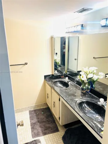 Extended vanity featuring dual oval undermount sinks, a dark stone countertop, light-toned cabinetry with metal hardware, and a full-width wall-mounted mirror