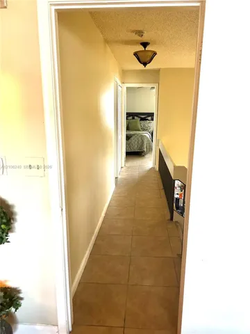 Hallway featuring tile flooring, ceiling-mounted light fixture, and black metal railing