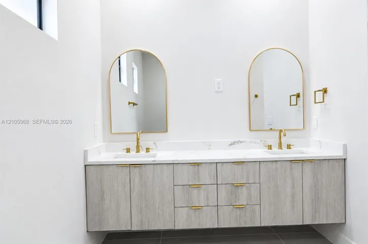 Floating vanity with wood-finish cabinetry, dual undermount sinks, stone-surface countertop, arched mirrors, and brass-tone fixtures