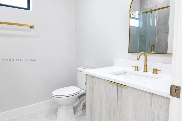 Vanity featuring light wood-finish cabinetry, a white countertop with an integrated rectangular sink, brass hardware, an arched mirror, and a wall-mounted faucet