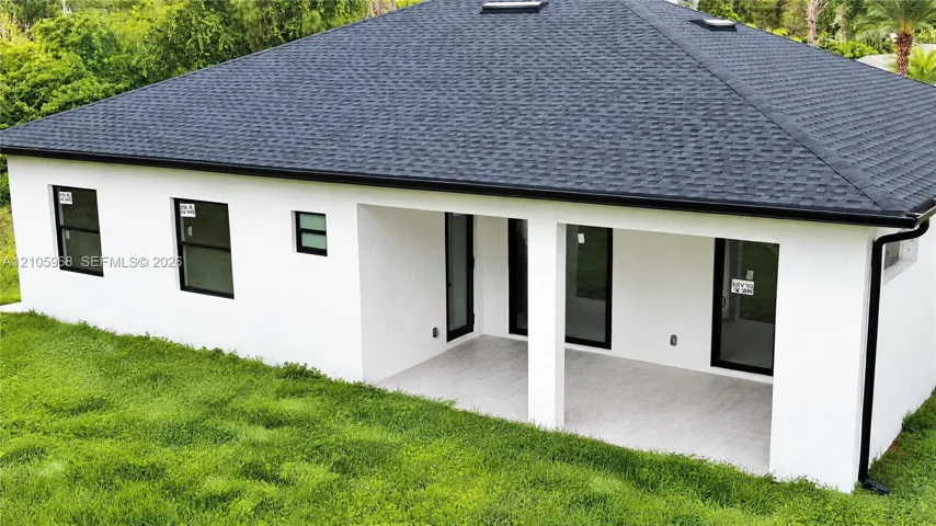 Stucco exterior featuring a covered patio, shingle roof with skylights, and dark-trimmed windows