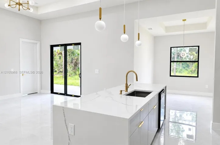 Kitchen island featuring a waterfall-edge countertop, undermount sink with a brass faucet, contemporary pendant lighting, light-tone cabinetry with gold-finish hardware, and large-format tile flooring