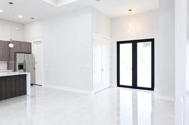 Open-concept interior featuring large-format polished tile flooring, high ceilings, a kitchen island with vertical wood-finish paneling, custom cabinetry, and black-framed glass-paneled double doors