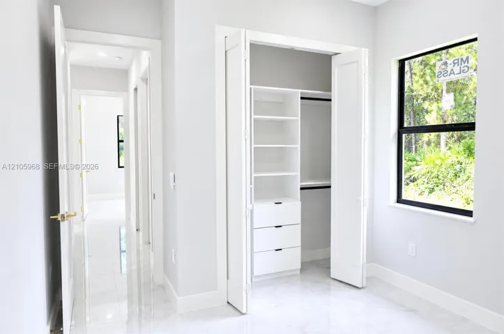 Custom closet featuring built-in shelving and drawers, large-format tile flooring, and black-framed window