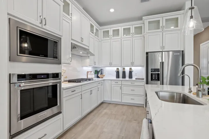 Kitchen featuring white shaker-style cabinetry with glass-front uppers, stainless steel appliances, stone countertops, and wood-finish flooring