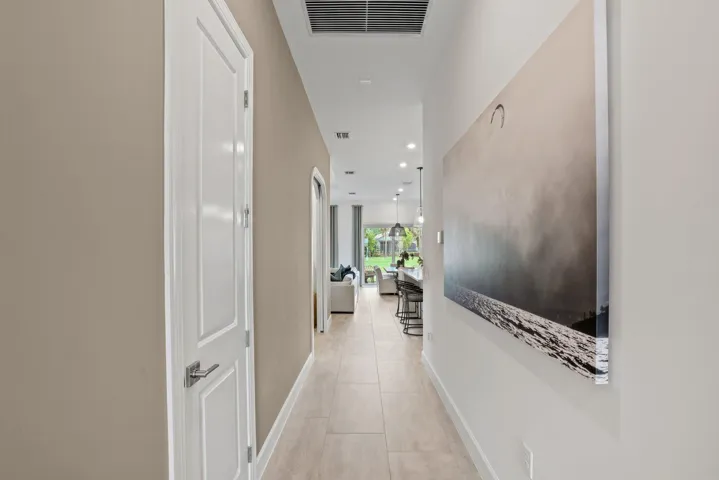 Interior hallway featuring large-format ceramic tile flooring, neutral wall paint, a multi-panel door with metallic hardware, and recessed lighting