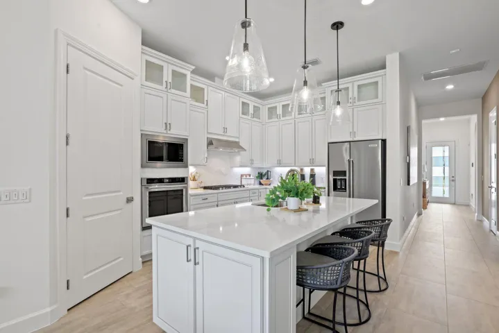 Kitchen featuring white shaker-style cabinetry with glass-front uppers, solid surface countertops, a central island, stainless steel appliances, and glass pendant lighting